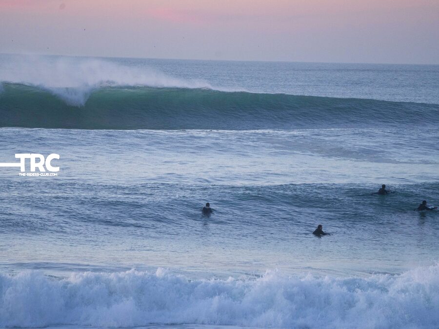 A group of surfers sitting in the lineup at dusk, waiting for waves
